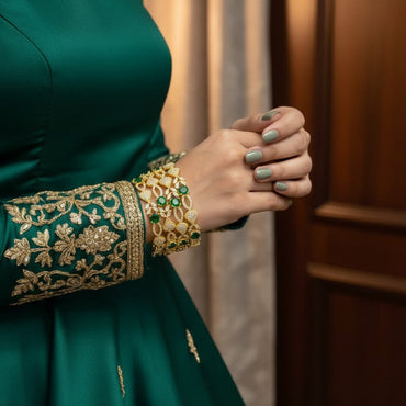 Green traditional outfit with gold embroidery and jewelry against a neutral background
