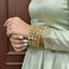 Close-up of a person wearing a light green dress with gold and turquoise jewelry against a brown background.