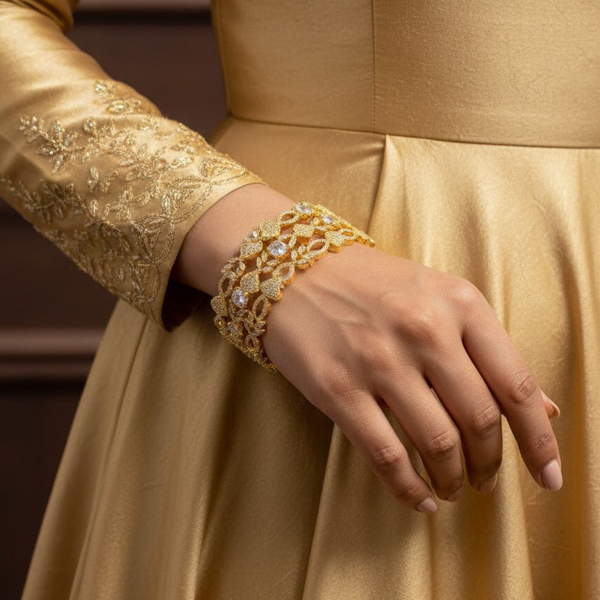 Gold dress with intricate detailing and a matching bracelet on a neutral background