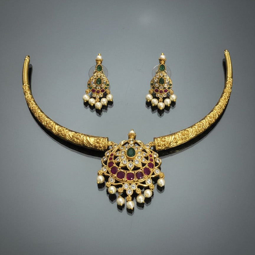 Gold necklace with emeralds, rubies, and pearls on a gray background