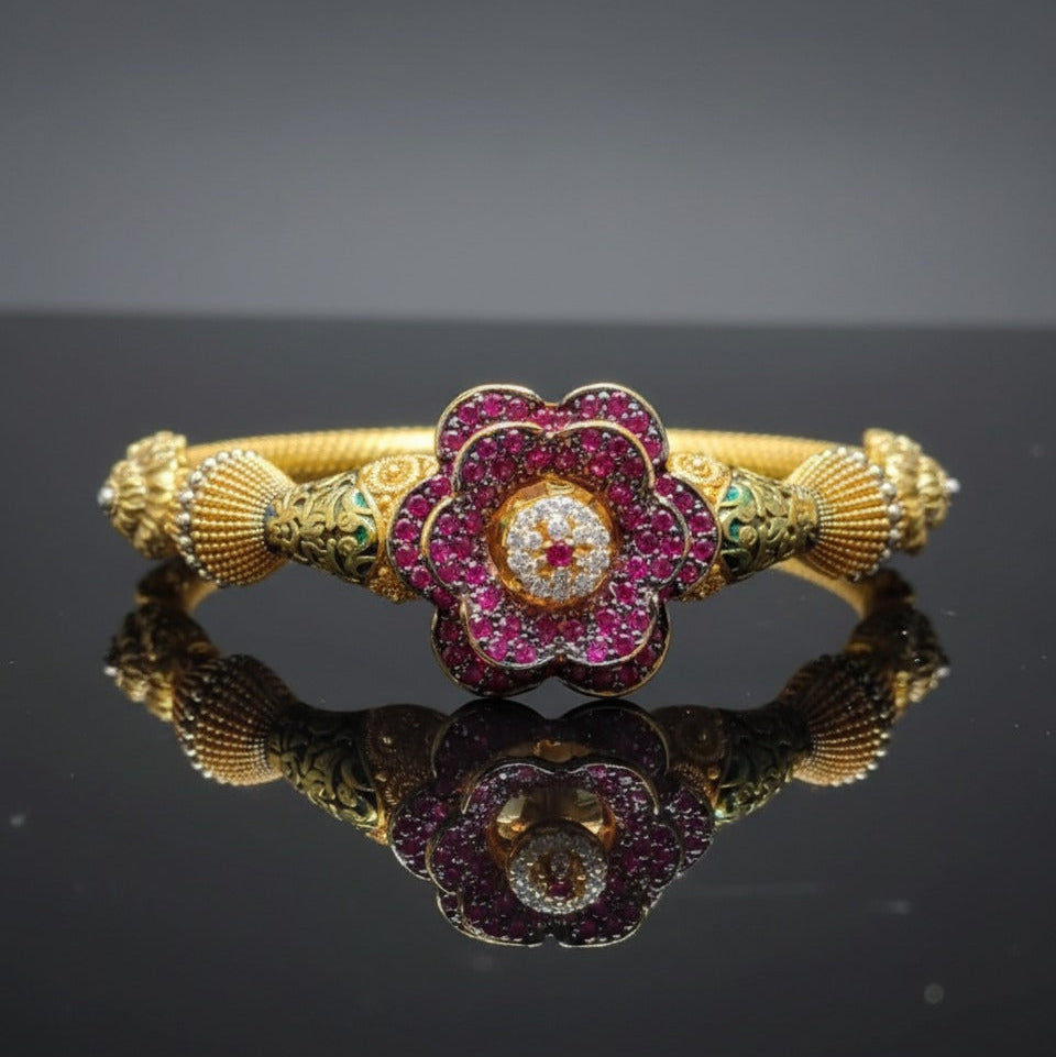 Gold bracelet with a floral design featuring red and green gemstones on a reflective surface.