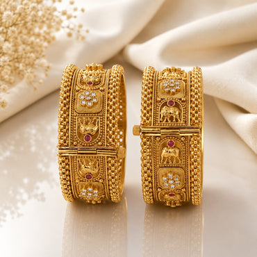 Gold-Tone Mughal Temple Granule Polki & Ruby CZ Wide Kada Bangle Set of 2 showing front and side panel detail on cream marble surface with baby's breath flowers backdrop