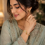 Woman wearing gold-tone Greek key meander dual bar open cuff bangle styled with a sage green embroidered Pakistani formal outfit and gold floral stud earrings
