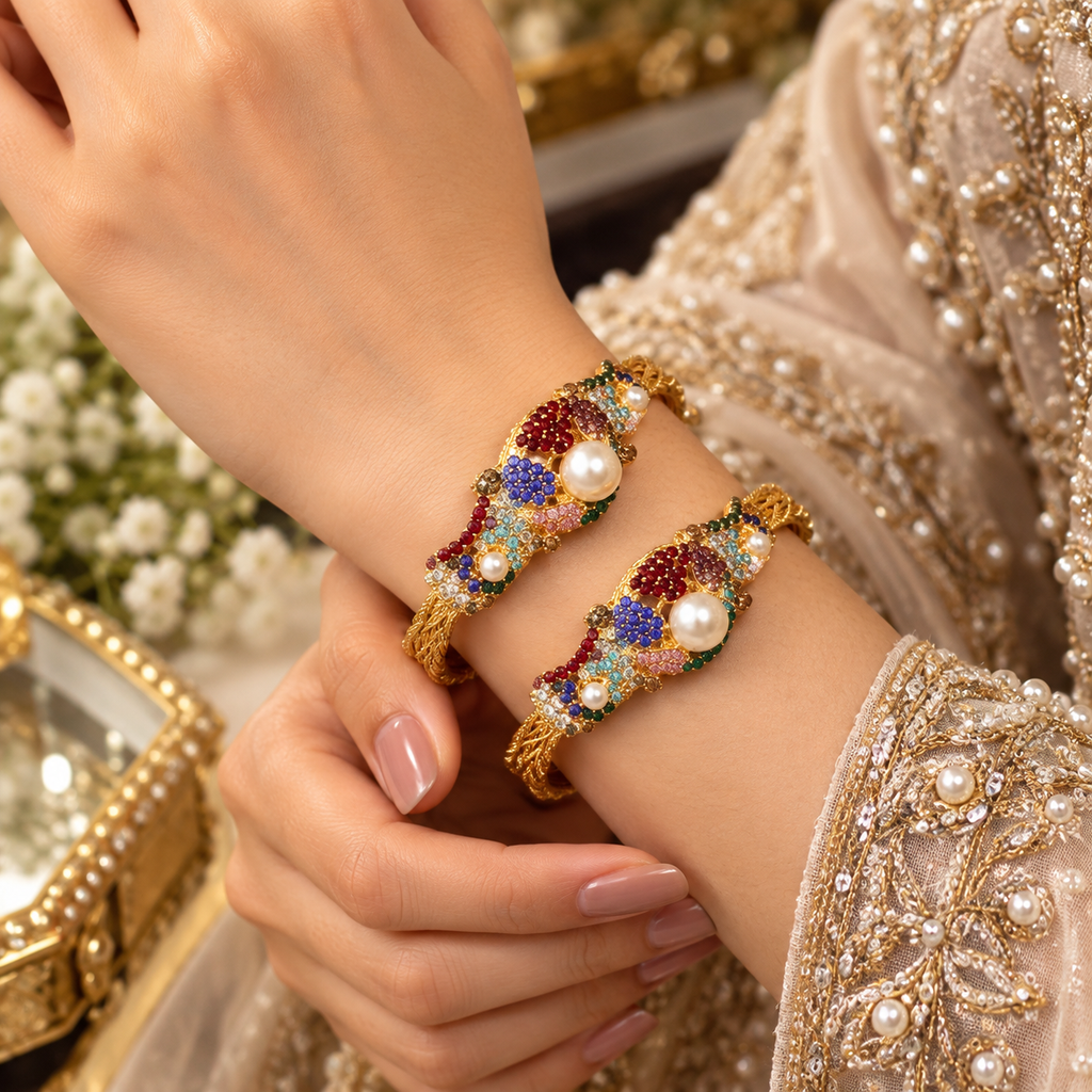 Woman wearing set of two gold-tone multicolour CZ and pearl traditional bridal bangles featuring ruby red royal blue emerald green pink aqua and white CZ floral clusters with cream pearl centrepiece on filigree mesh band styled with ivory pearl-embellished Pakistani bridal outfit