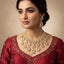 Woman wearing a red traditional outfit with gold jewelry against a beige background