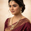 Woman wearing a maroon saree with gold jewelry against a beige background