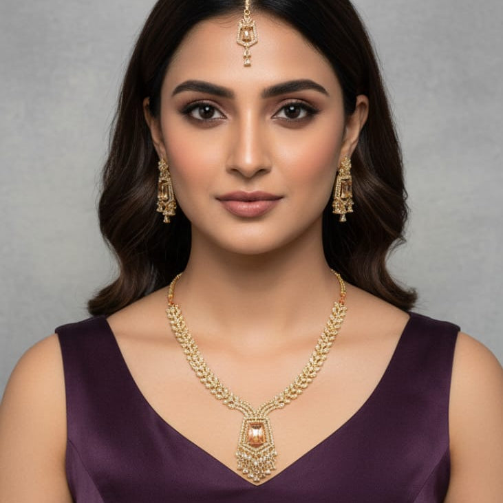 Woman wearing gold jewelry including a necklace, earrings, and a bindi against a gray background