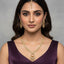 Woman wearing gold jewelry including a necklace, earrings, and a bindi against a gray background