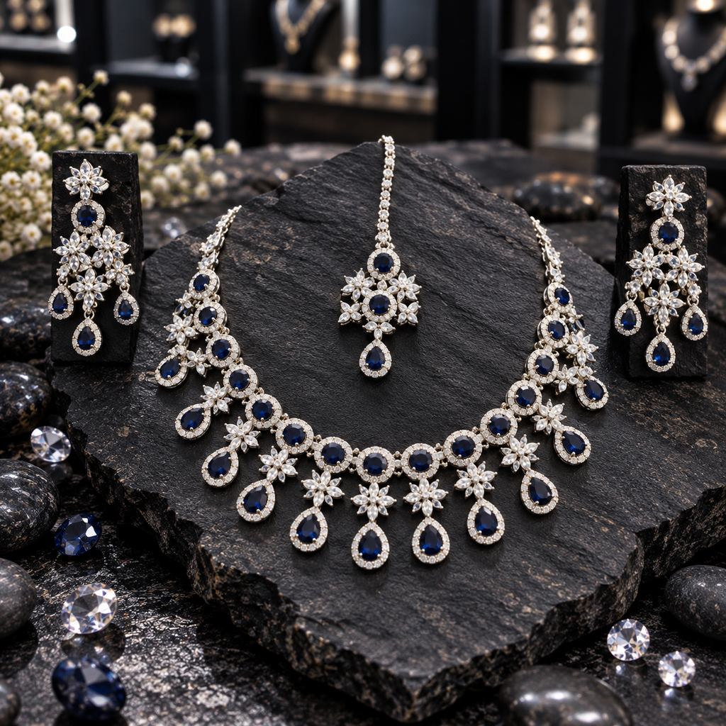 Silver-tone AD necklace with dark blue round halos, clear flower clusters and blue teardrop drops, displayed with matching chandelier earrings and maang tikka on dark slate.