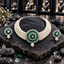 Cream pearl-look multi-strand choker with a round green-accent medallion, clear concentric borders, a floral centre and pearl-look drop, displayed with matching round green drop earrings on dark slate.