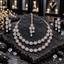 Silver-tone AD double-layer necklace with light pink oval halo accents, displayed with matching clear-teardrop earrings and maang tikka on dark slate.