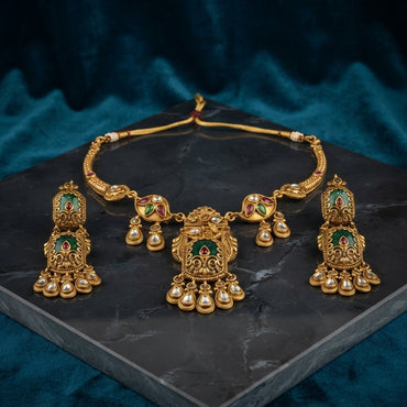 Antique Gold Kundan Temple Pendant Torque Necklace & Jhumka Earrings Bridal Set on dark grey marble surface with teal blue velvet drape backdrop