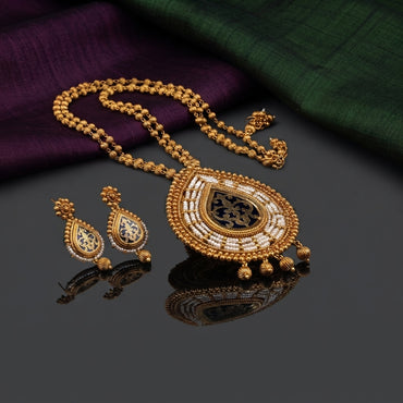 Antique Gold Meenakari Teardrop Pearl Pendant Long Necklace Earrings Set on dark grey mirror surface with purple and green silk fabric backdrop showing double-strand ribbed gold ball bead chain with large teardrop pendant featuring concentric micro seed pearl rows antique gold bead border black meenakari enamel centre with arabesque gold cutwork and gold bead drop fringe alongside matching smaller teardrop drop earrings with mirror reflections below