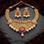 Antique Gold Ruby Pearl Mughal Filigree Bridal Choker Necklace Earrings Set on dark slate stone surface with burgundy velvet fabric backdrop showing wide mesh jali antique gold bib choker with dense filigree arabesque scroll work top row of oval polki uncut CZ stones large ruby garnet cabochon centre pendant with emerald centre faux pearl drop and cascading round faux pearl drops along base with matching gold filigree chandbali earrings featuring oval ruby CZ cabochon and four faux pearl drops