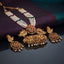 Antique Gold Temple Dabba Pendant Seed Pearl Necklace Earrings Set on dark grey mirror surface with purple and teal silk fabric backdrop showing 5-strand white seed pearl chain with silk knot spacers and large antique gold temple cylinder dabba pendant with ruby red kundan CZ floral top emerald green CZ scrollwork peacock motifs and faux pearl drop fringe alongside matching antique gold floral disc stud earrings with ruby red pear kundan CZ petals and pearl drops