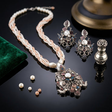 Antique Silver-Tone Multicolor CZ Pavé Baroque Floral Lotus Pendant on Multi-Strand Twisted Seed Pearl & Rose Bead Long Necklace & Stud Earrings Set on black mirror surface with loose freshwater pearls, green velvet pouch and antique silver perfume bottle backdrop