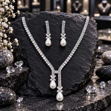 Full view of a necklace and earrings set with rectangular clear accents, four-petal motifs and white teardrop pearl-look drops.