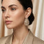 Baguette CZ Teardrop Stud Earrings with Round Pavé Border in silver-tone plating flat lay on black mirror surface with dark silk backdrop showing pair of open teardrop studs with tiered channel-set baguette CZ interior and micro-pavé round CZ border with mirror reflections below