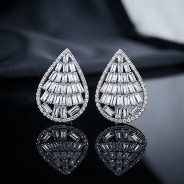 Baguette CZ Teardrop Stud Earrings with Round Pavé Border in gold-tone plating flat lay on dark grey stone surface with dark silk backdrop showing pair of open teardrop studs with tiered channel-set baguette CZ interior and micro-pavé round CZ border with mirror reflections below