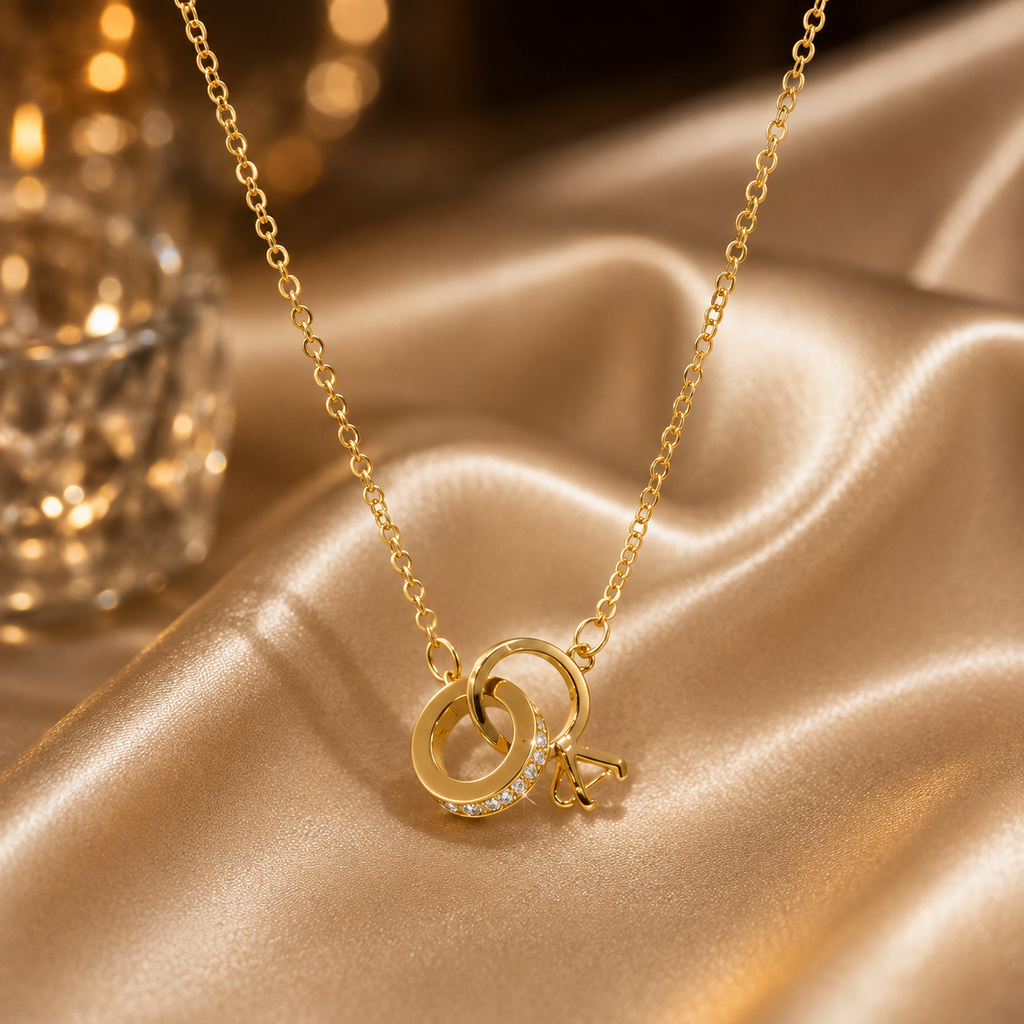 Gold-tone interlocking double rings CZ pendant necklace with geometric triangle charm drop on fine cable chain displayed on golden satin fabric