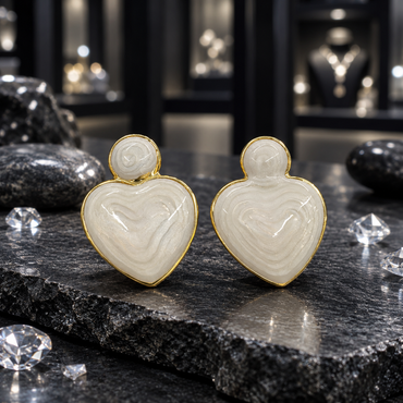 Pair of cream heart-shaped earrings with small round tops, glossy swirled surfaces and gold-tone borders displayed on dark slate.