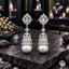 Pair of silver-tone jhumka earrings with clear oval accents, sparkling bell-shaped tiers and large white pearl-look drops.