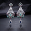 CZ Baguette Fan and Multicolour Sunburst Peacock Drop Earrings in Silver Multicolour worn by model in cream outfit with ornate backdrop close-up detail showing rhodium silver baguette cone fan peacock spoke fan with multicolour oval CZ accents and sapphire blue pear halo drop