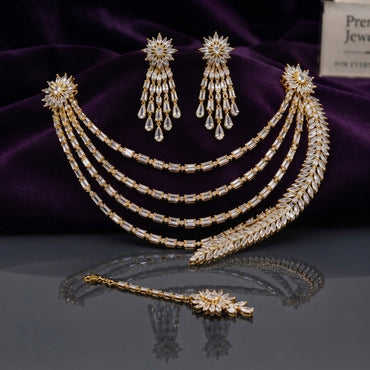 CZ Bridal Multi-Layer Drape Necklace Set with Starburst Brooch in Gold flat lay on dark surface with purple velvet backdrop showing 4-strand draped CZ tennis chains with twin starburst shoulder brooches matching tassel drop earrings and maang tikka in champagne gold-tone with white CZ