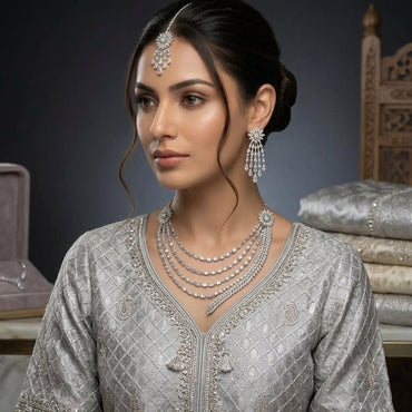 CZ Bridal Multi-Layer Drape Necklace Set with Starburst Brooch in Silver model wear editorial showing South Asian bride wearing 4-strand draped CZ necklace with starburst shoulder brooch matching starburst tassel earrings and maang tikka with rhodium silver finish on grey embroidered outfit