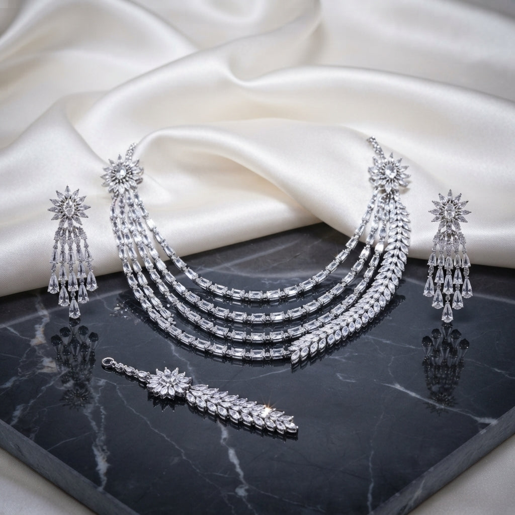 CZ Bridal Multi-Layer Drape Necklace Set with Starburst Brooch in Silver flat lay on dark marble surface showing 4-strand draped CZ tennis chains with twin starburst shoulder brooches matching tassel drop earrings and maang tikka in rhodium silver with white CZ
