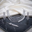 CZ Bridal Multi-Layer Drape Necklace Set with Starburst Brooch in Silver flat lay on dark marble surface showing 4-strand draped CZ tennis chains with twin starburst shoulder brooches matching tassel drop earrings and maang tikka in rhodium silver with white CZ