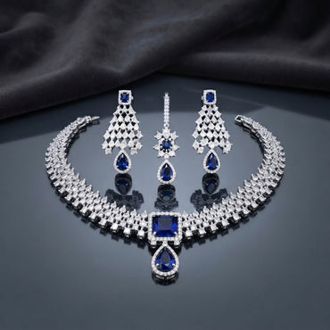 CZ Diamond Bridal Choker Necklace Earrings Maang Tikka Set in Emerald Green showing wide pave CZ tennis choker collar with large cushion and pear emerald green CZ centre pendant matching long chandelier earrings with geometric lattice panel and pear drop and maang tikka on dark mirror surface with charcoal satin backdrop