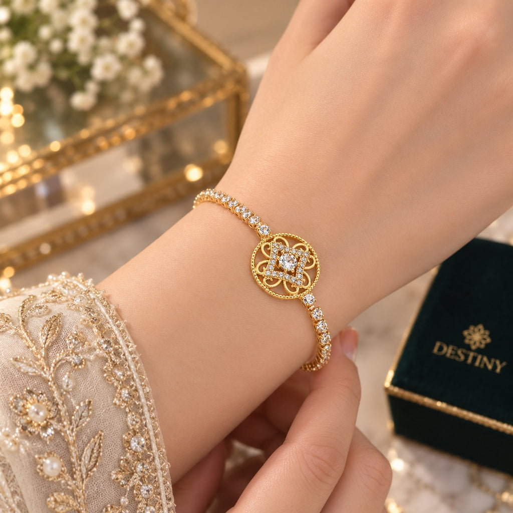 CZ Filigree Arabesque Medallion Centrepiece Round CZ Tennis Chain Bracelet in gold-tone worn on model wrist in bridal embroidered outfit with Destiny jewelry box and floral backdrop