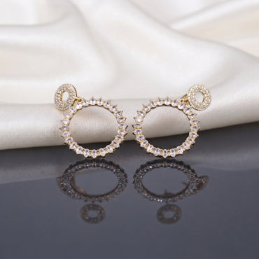 CZ Marquise Circle Drop Earrings with Pave Disc Top in Gold pair lying side by side on dark mirror surface with white satin fabric backdrop showing 18K champagne gold-tone fully pave CZ open-circle disc stud top suspending large open circle drop fully encrusted with radial marquise CZ in crown sunburst arrangement with mirror reflection below