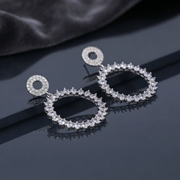 CZ Marquise Circle Drop Earrings with Pave Disc Top in Silver pair lying on dark slate mirror surface with dark silk backdrop showing rhodium-plated fully pave CZ open-circle disc stud top suspending large open circle drop fully encrusted with radial marquise CZ in crown sunburst arrangement with mirror reflection below