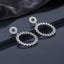 CZ Marquise Circle Drop Earrings with Pave Disc Top in Silver pair lying on dark slate mirror surface with dark silk backdrop showing rhodium-plated fully pave CZ open-circle disc stud top suspending large open circle drop fully encrusted with radial marquise CZ in crown sunburst arrangement with mirror reflection below