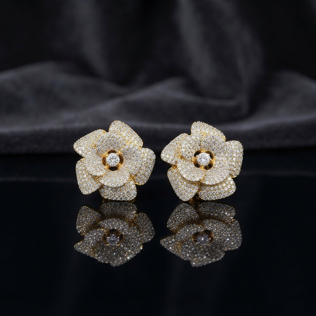 CZ Micro-Pavé 3D Camellia Rose Flower Stud Earrings in 22K Gold on black mirror surface with dark grey silk fabric backdrop