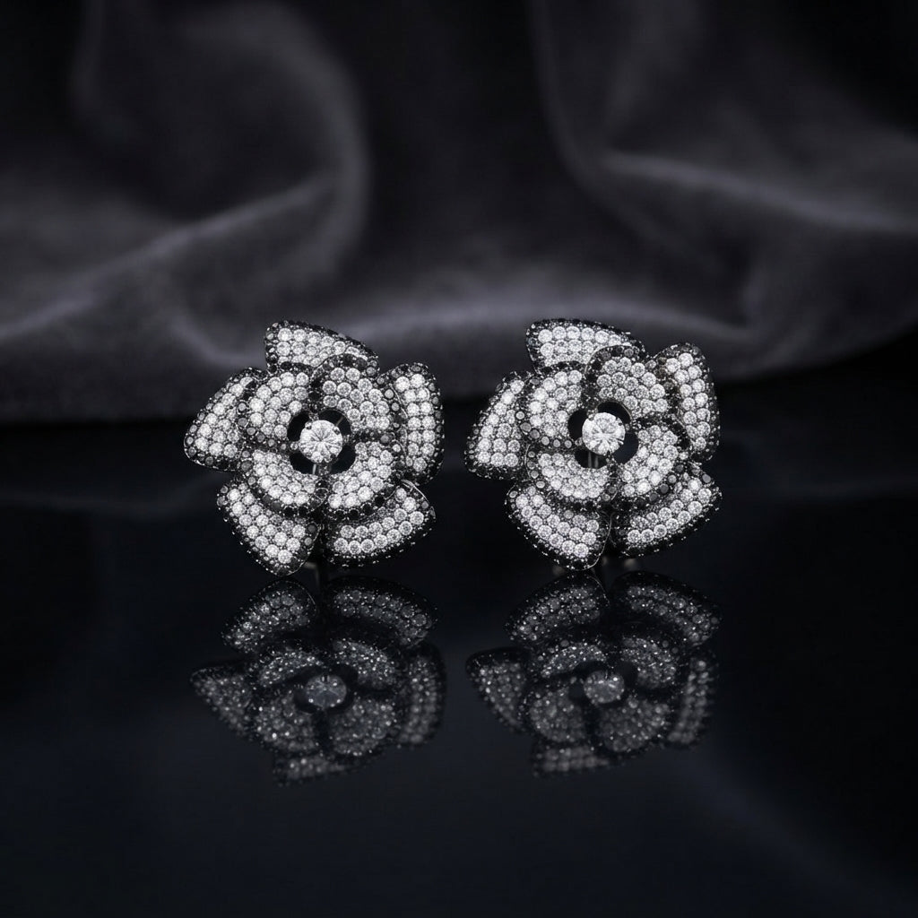 CZ Micro-Pavé 3D Camellia Rose Flower Stud Earrings in Black & Silver on black mirror surface with dark smoke fabric backdrop