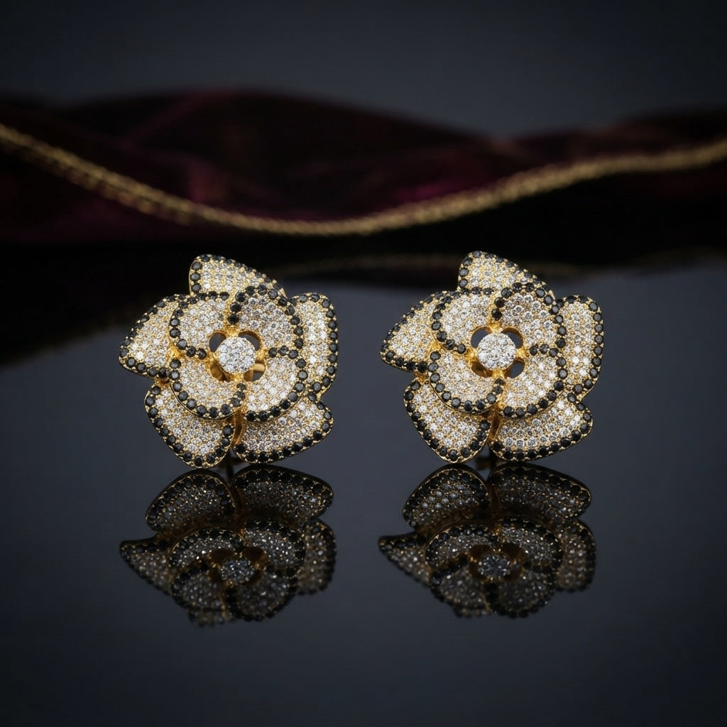 CZ Micro-Pavé 3D Camellia Rose Flower Stud Earrings in Gold & Black on dark mirror surface with deep burgundy velvet fabric backdrop