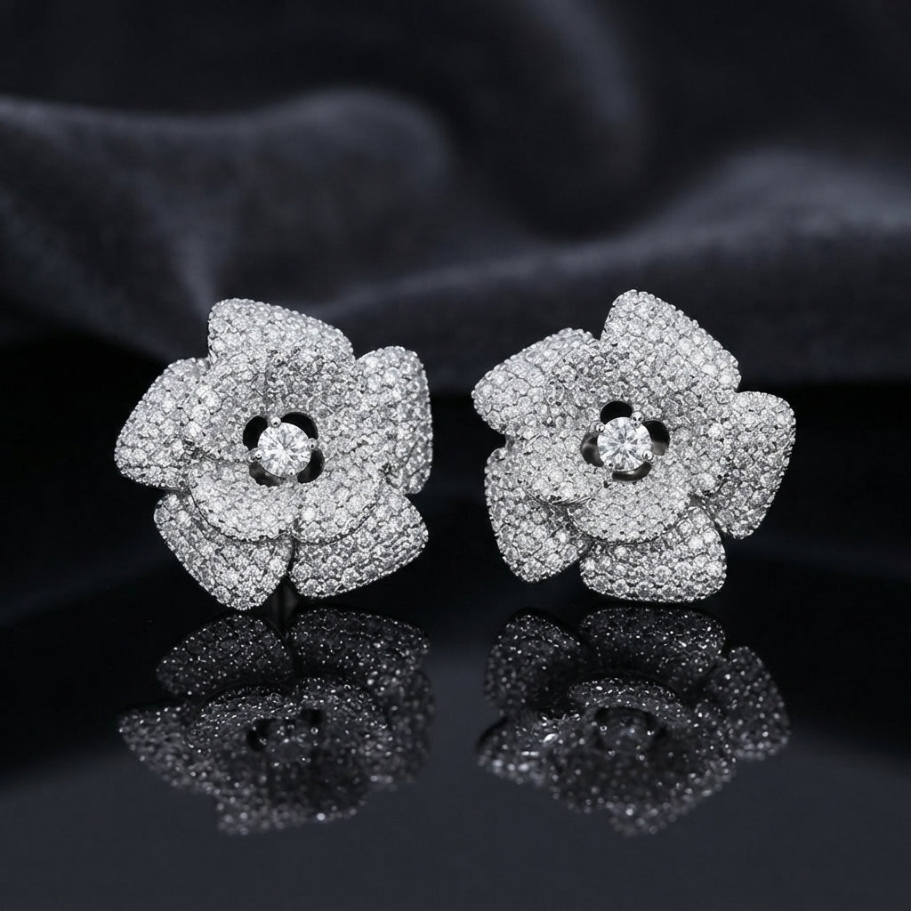 CZ Micro-Pavé 3D Camellia Rose Flower Stud Earrings in Silver on black mirror surface with dark grey silk fabric backdrop