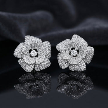 CZ Micro-Pavé 3D Camellia Rose Flower Stud Earrings in Silver on black mirror surface with dark grey silk fabric backdrop