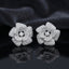 CZ Micro-Pavé 3D Camellia Rose Flower Stud Earrings in Silver on black mirror surface with dark grey silk fabric backdrop