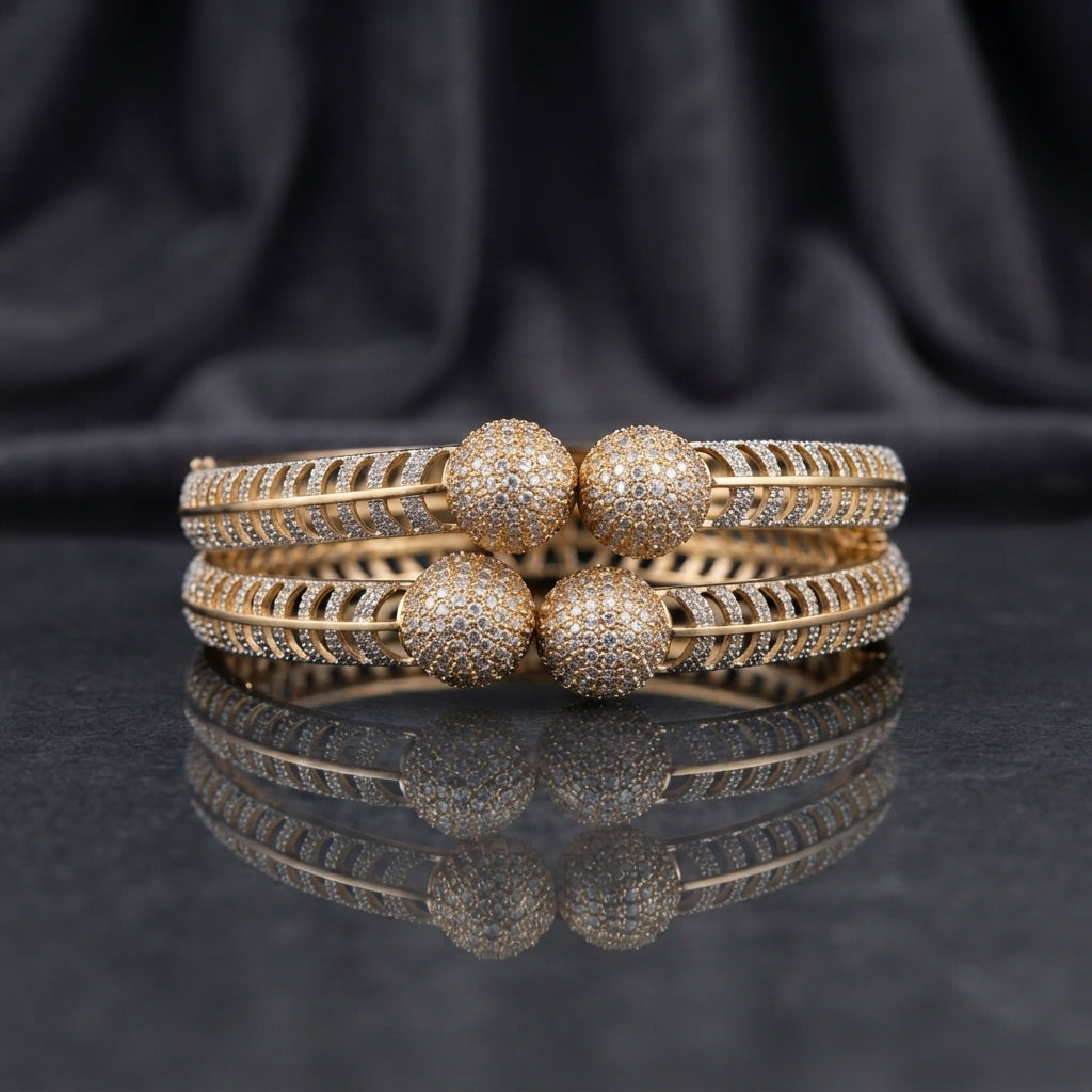 CZ Pave Ball Charm Multi-Row Open-Work Spine Bangle Pair in gold-tone finish displayed stacked on dark grey marble mirror surface with black silk drape backdrop showing two matching bangles with double-row chevron herringbone spine-rib lattice band continuous round CZ micro-pave and 4 large round CZ pave ball charms at center front with mirror reflection below