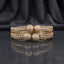 CZ Pave Ball Charm Multi-Row Open-Work Spine Bangle Pair in gold-tone finish displayed stacked on dark grey marble mirror surface with black silk drape backdrop showing two matching bangles with double-row chevron herringbone spine-rib lattice band continuous round CZ micro-pave and 4 large round CZ pave ball charms at center front with mirror reflection below