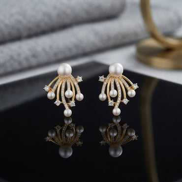 CZ Pave Multi-Pearl Firework Spray Stud Earrings in Gold pair on black square tray with grey marble and gold prop backdrop showing 18K gold-tone large pearl centre stud with 6-7 fully CZ pave curved wire arms in firework spray fan with small pearl finials and round CZ accent stones with mirror reflection below