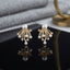 CZ Pave Multi-Pearl Firework Spray Stud Earrings in Gold pair on black square tray with grey marble and gold prop backdrop showing 18K gold-tone large pearl centre stud with 6-7 fully CZ pave curved wire arms in firework spray fan with small pearl finials and round CZ accent stones with mirror reflection below