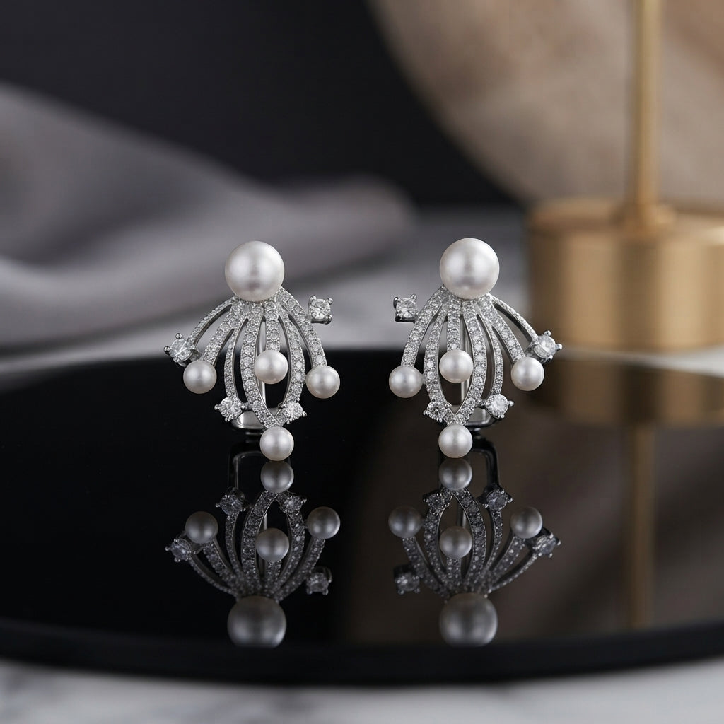 CZ Pave Multi-Pearl Firework Spray Stud Earrings in Silver pair on black oval tray with grey silk and gold prop backdrop showing rhodium-plated large pearl centre stud with 6-7 fully CZ pave curved wire arms in firework spray fan with small pearl finials and round CZ accent stones with mirror reflection below