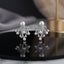 CZ Pave Multi-Pearl Firework Spray Stud Earrings in Silver pair on black oval tray with grey silk and gold prop backdrop showing rhodium-plated large pearl centre stud with 6-7 fully CZ pave curved wire arms in firework spray fan with small pearl finials and round CZ accent stones with mirror reflection below