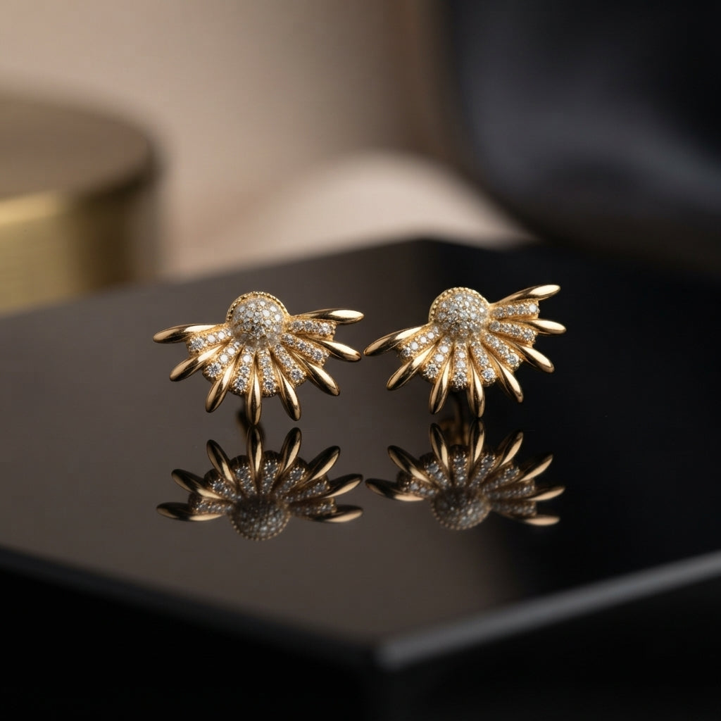 CZ Pave Sunburst Fan Stud Earrings in Gold pair on black lacquer surface with warm gold backdrop showing 18K gold-tone bold statement studs with fully pave CZ domed ball centre and 10-12 slim tapered rays with CZ-filled fan body with mirror reflection below