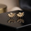 CZ Pave Sunburst Fan Stud Earrings in Gold pair on black lacquer surface with warm gold backdrop showing 18K gold-tone bold statement studs with fully pave CZ domed ball centre and 10-12 slim tapered rays with CZ-filled fan body with mirror reflection below